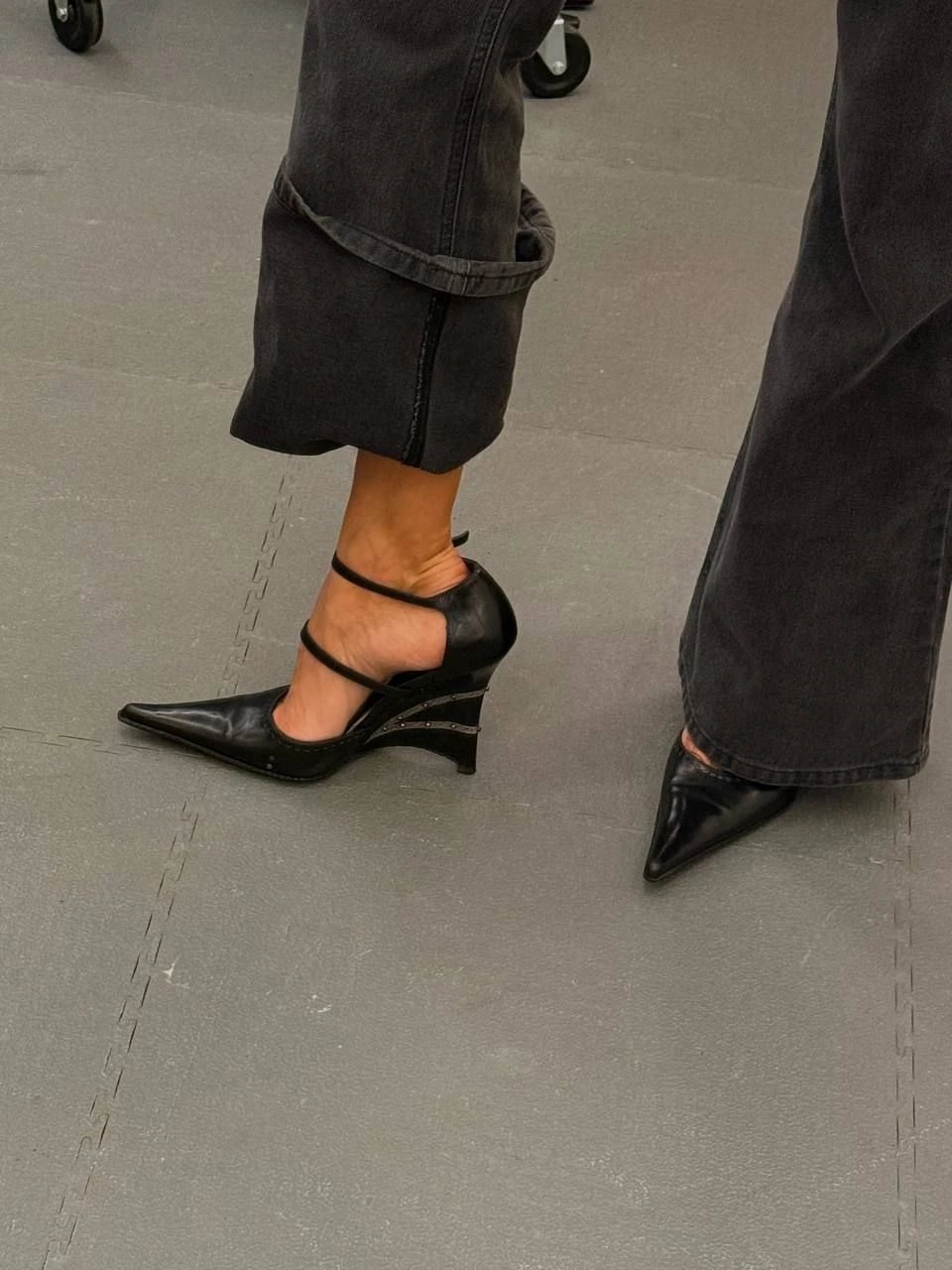 Detalj av svarta spetsiga skor och mörka jeans.